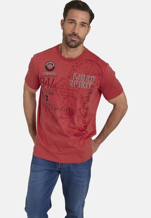 Red cotton t-shirt with short sleeves, featuring printed text and map patterns. Paired with blue jeans for a casual look.