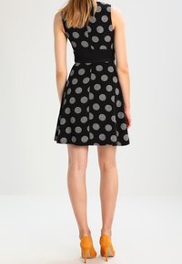 Musta mekko valkoisilla pilkuilla, olkaimeton muotoilu, laahustava malli. Yhdistetty oransseihin korkeakorkoisiin kenkiin, sileä kangastuntuma.