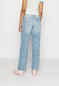Jeans azul claro com padrão em espiral, de cintura alta, corte relaxado e dois bolsos traseiros. Combinados com sapatos chunky em rosa pálido.