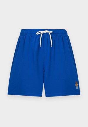 Blå badebukser med hvit snor og liten brodert bjørnelogo på nedre høyre ben, vist mot en ensfarget bakgrunn.