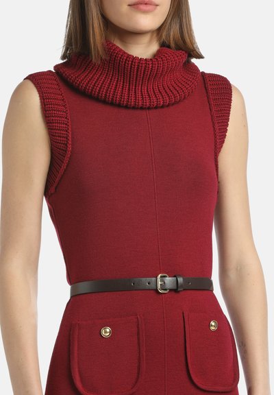 Rdeča brezrokavnica z velikim, rebrastim ovratnikom in teksturiranimi detajli na rame. Ima črn usnjen pas in sprednje žepe z zlatimi gumbi.
