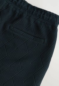 Tissu à motif sombre avec un design géométrique et une taille élastique. Comprend une poche passepoilée à l'arrière.