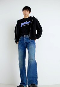 Jeans de mezclilla azul de pierna acampanada con un ajuste de altura media, combinados con una camiseta gráfica negra y una sudadera con cremallera negra. Textura suave, diseño casual.