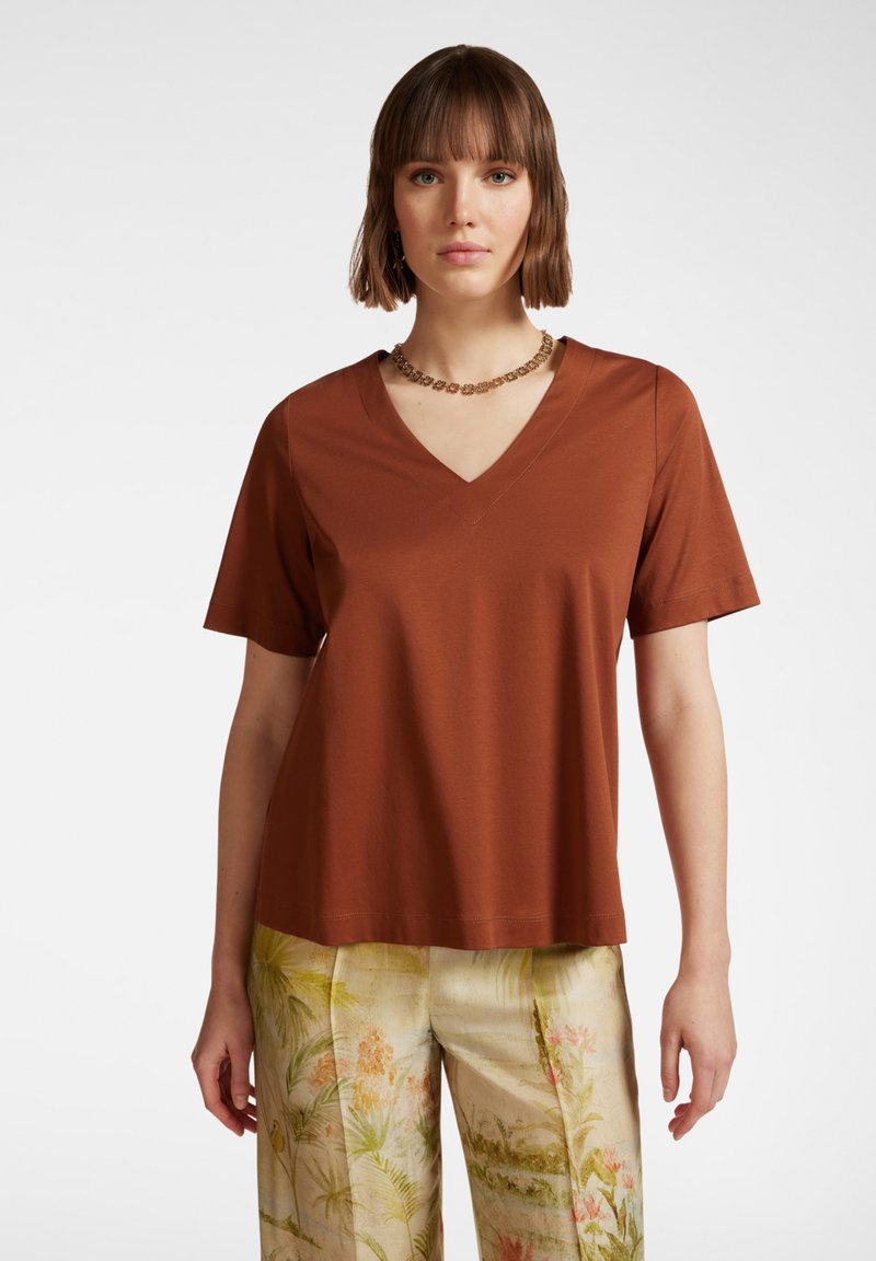 Top corto a maniche corte color ruggine con scollatura a V, realizzato in tessuto morbido, caratterizzato da una vestibilità ampia e dettagli di cucitura puliti. Abbinato a pantaloni a fantasia.