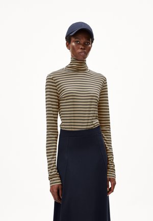 Maglione a collo alto a righe beige e grigio scuro, abbinato a una gonna blu. La modella indossa un cappello blu, sottolineando un look rilassato.