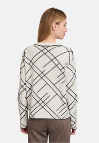 Cremefarbener Pullover mit schwarzem geometrischen Muster. Weiche Textur, runder Ausschnitt, überschnittene Schultern und gerippte Bündchen. Lässiger, entspannter Schnitt.