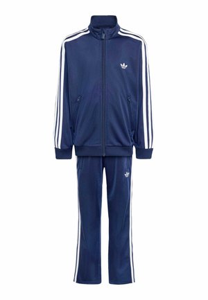 Mørkeblå Adidas træningsdragt med hvide striber på ærmer og bukser, lynlåstrøje og Adidas trefoil logoer på bryst og lår.