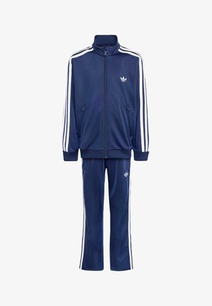 Mørkeblå Adidas træningsdragt med hvide striber på ærmer og bukser, lynlåstrøje og Adidas trefoil logoer på bryst og lår.