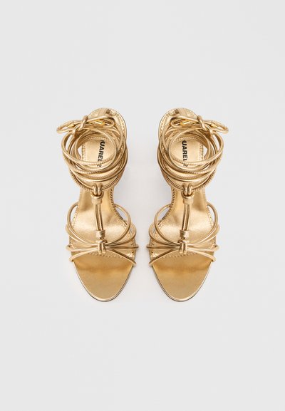 Gouden sandalen met hoge hakken, voorzien van meerdere verstrengelde banden, een gladde textuur, vierkante open teen en een slanke stilettohak.