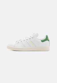 Weiße Adidas Stan Smith Sneaker mit grünem Fersenbereich, perforierten Streifen und beiger Sohle, seitlich auf einem weißen Hintergrund abgebildet.