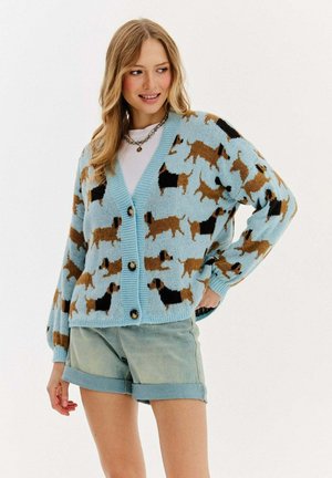 Sweter typu cardigan w jasnoniebieskim kolorze, z brązowym i czarnym wzorem w psy. Zawiera duże guziki i luźny krój.