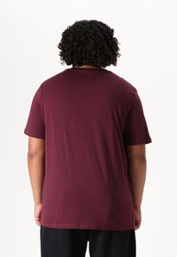 Burgundowa bawełniana koszulka z krótkimi rękawami, okrągłym dekoltem i gładką fakturą, widziana od tyłu. Prosty design, bez widocznych wzorów.