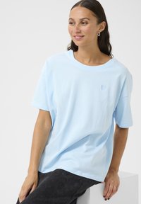 Light blue cotton t-shirt with a round neckline, short sleeves, and a small embroidered heart detail on the chest. Soft texture.