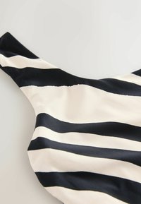 Juodai baltos juostelės audinys su lygiu paviršiumi, turintis plačias pakaitines juostas. Dizainas apima išlenktą iškirptę ir pečių dirželius.