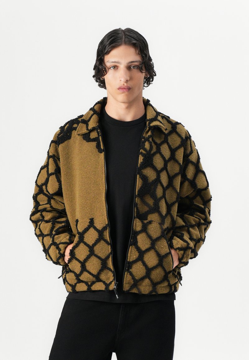 Fleece zip-up jacket in olive green with a black geometric pattern, featuring a collar and side pockets. Textured fabric provides warmth.