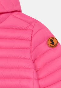 Pink puffer jacket with horizontal stitching, featuring a round orange patch with a black silhouette on the left shoulder. Smooth texture.