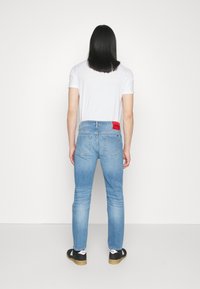 Jeans de denim azul claro con corte slim, que presentan un parche de logo rojo en la parte trasera de la cintura y un diseño clásico de cinco bolsillos.