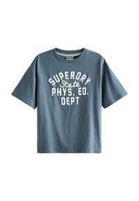 Modré bavlněné tričko s kulatým výstřihem a krátkými rukávy. Na přední straně je vytištěn tučný bílý text: "SUPERDRY Stát FYZ. ED. ODDĚLENÍ".