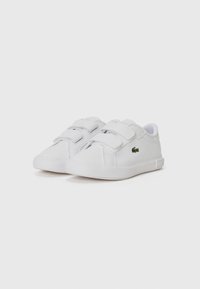Baskets blanches avec deux bandes Velcro, tige en cuir lisse, col rembourré et petit emblème vert. Semelle en caoutchouc texturé pour une meilleure adhérence.