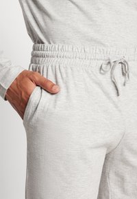 Pantalones jogger de color gris claro, fabricados con una tela suave y texturizada. Cuentan con una cintura elástica con cordón y bolsillos laterales.
