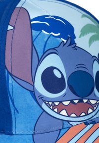 Gorra azul con un personaje de dibujos animados de grandes ojos y una amplia sonrisa, rodeado de una colorida escena de playa y acentos tropicales.