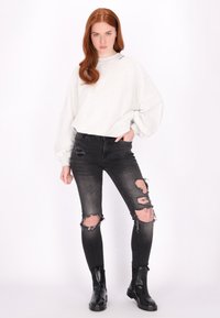 Felpa oversize grigia chiara con scollatura a coste, abbinata a jeans skinny neri con ginocchia strappate e stivaletti neri alla caviglia.