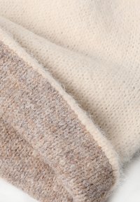 Gestrickte Mütze in hellbeige und sanften Tan-Tönen. Verfügt über eine strukturierte Oberfläche mit einem umgeschlagenen Saum. Der Stoff wirkt warm und kuschelig.