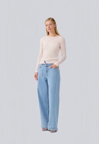 Uma blusa de manga longa rosa clara combinada com umas calças largas de ganga azul claro com cintura ajustável e bolsos laterais.