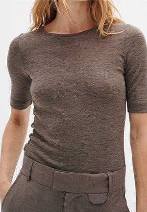 Mujer con una camiseta marrón ajustada de manga corta metida dentro de pantalones marrones de cintura alta con un cinturón ancho.