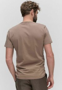 T-shirt z krótkim rękawem w jednolitym jasnobrązowym kolorze, wykonany z miękkiego materiału. Posiada okrągły dekolt i luźny krój, bez widocznych wzorów czy dodatków.