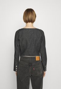 Veste en denim noir courte avec des manches longues et des accents en bouton. Présente un col carré et une texture lisse, associée à un jean foncé.