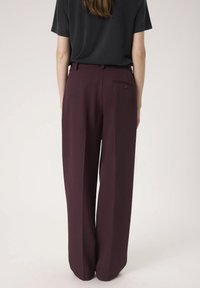 Burgunderfarbene weit geschnittene Hose mit glatter Oberfläche, die über eine Gesäßtasche und eine taillierte Passform verfügt, kombiniert mit einem schwarzen kurzärmeligen Oberteil.
