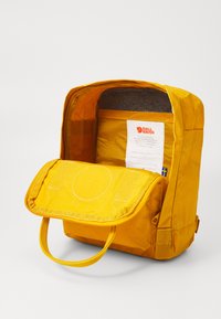 Κίτρινος υφασμάτινος σακίδιο με καπάκι, άνω χερούλι και εσωτερική ετικέτα. Υφασμάτινη επένδυση, απλός σχεδιασμός και ασφαλής μηχανισμός κλεισίματος.