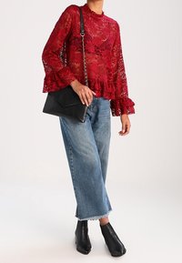 Rød blondebluse med lange flæseærmer, parret med højttaljede lyseblå denimjeans. Sort crossbody taske og ankelstøvler.