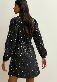 Zwarte jurk met een sterrenprint in het wit, lange mouwen met gathered manchetten en een taillekoord voor een getailleerd silhouet.