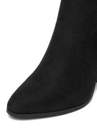 Stivaletto alto in suede nero con punta affusolata e suola liscia, mostrato da un'angolazione laterale ravvicinata.