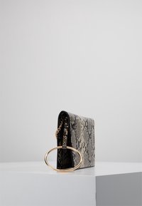 Sac en simili cuir imprimé serpent avec une forme structurée, des accessoires ronds en or et une bandoulière en chaîne. Le motif texturé présente des nuances de beige et de noir.