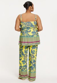Kleurige twee-delige outfit met een gele top met een peplum taille en bedrukte turkooise broek met paarse en groene accenten.