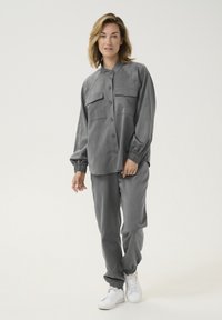 Gray shirt with button closure and two chest pockets, paired with matching pants. Both garments have elastic cuffs and a relaxed fit.