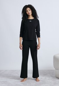 Mustast pehmest kangast pikkade varrukatega topp ja laiade pükstega püksid. Topil on rinnal väike tikitud logo. Lihtne disain.