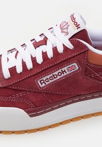 Adidași Reebok cu un superior din suede burgund, șireturi albe și un accent contrastant de bej. Beneficiază de o talpă intermediară groasă albă și o talpă exterioară din cauciuc gumos.
