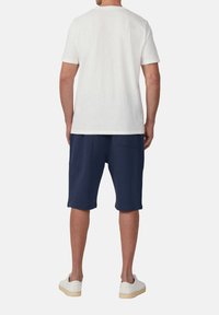 Herenoutfit met een effen witte T-shirt met korte mouwen en marineblauwe shorts. De schoenen zijn wit met een gestructureerde zool. Casual ontwerp.