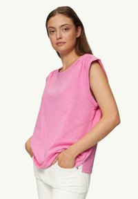 Roze mouwloze top met een ronde halslijn en plooiwerking bij de schoudernaden. Gemaakt van een zachte, lichte stof, gecombineerd met witte broek.