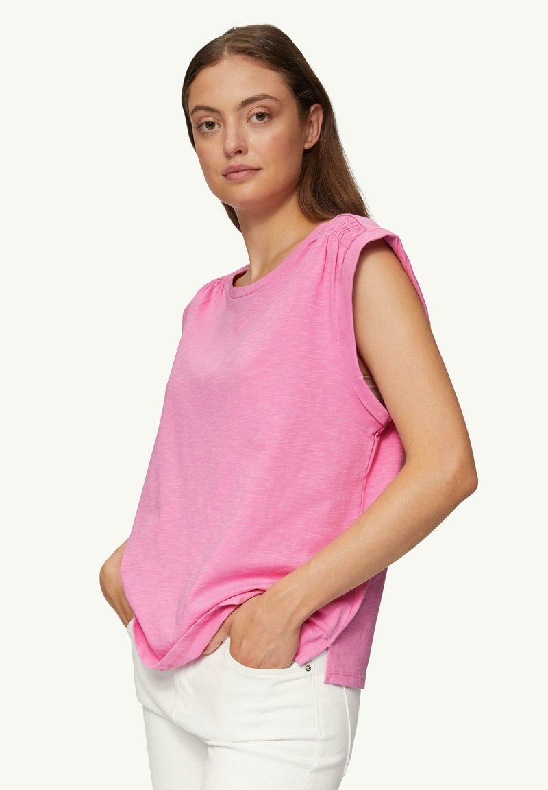 Roze mouwloze top met een ronde halslijn en plooiwerking bij de schoudernaden. Gemaakt van een zachte, lichte stof, gecombineerd met witte broek.