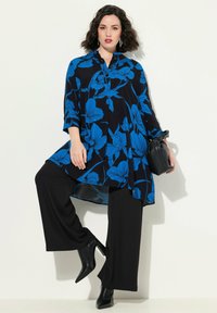 Czarna tunika z niebieskim wzorem kwiatowym, zestawiona z czarnymi spodniami o szerokich nogawkach i czarnymi czółenkami na obcasie. Tunika ma zapięcie na guziki przy dekolcie i rękawy o długości trzech czwartych.