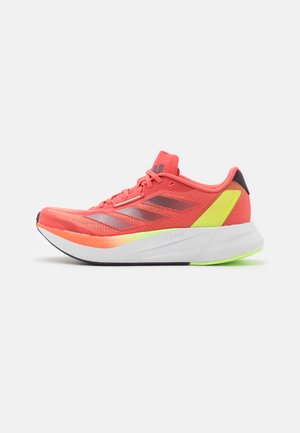 Zapatilla de running en coral brillante con rayas gris oscuro, con una parte superior de malla, amortiguación ligera y una suela colorida con un acento prominente.