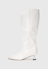 Bota blanca hasta la rodilla con textura de cocodrilo, punta afilada y tacón bajo curvado sobre un fondo blanco liso.