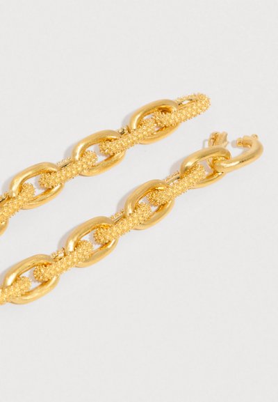 Arany tónusú láncszem fülbevalók, váltakozó sima és texturált szemekkel, egyszínű fehér háttér előtt.