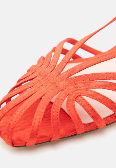 Κόκκινο σανδάλι με λουράκια και πολλούς υφασμάτινους ιμάντες που διασταυρώνονται πάνω από τα δάχτυλα και ανοιχτό σχέδιο σε ανοιχτό φόντο.