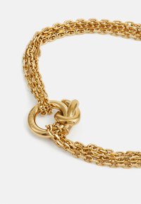 Goldene Mehrfachkette mit ineinandergreifenden Gliedern, einer strukturierten Oberfläche und einem auffälligen runden Toggle-Verschluss. Ideal zum Schichten.